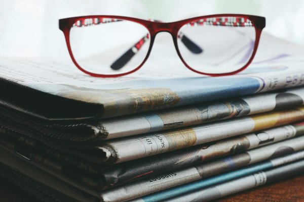 A pair of reading glasses resting on a stack of newspapers.
